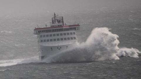 The Manxman ferry, which is white, red and black, hitting a wave in rough seas.