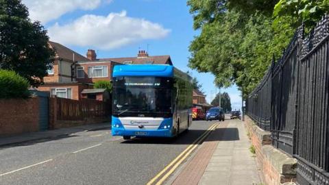 Blue Stagecoach bus driving along road on sunny day with trees on both sides.