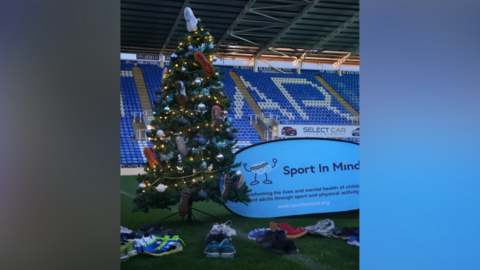 A Christmas tree decorated with trainers on the pitch in front of the stand at Reading FC's stadium