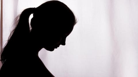 A side-on silhouette of a woman, she has her head bowed and is wearing her hair in a pony-tail.
