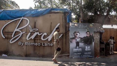 A group of police officials stand outside the premises of the Birch By Romeo Lane nightclub in northern Goa where a deadly blaze killed 25 people in the early hours of Sunday. The main wall has the name of the nightclub, beside that there's a poster of some music performances held on 5th and 6th December