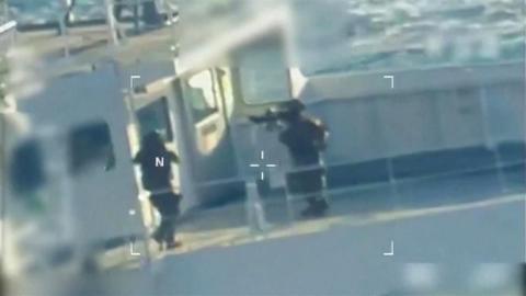 A US strike team with guns walk on a boat. A white target outline is shown over the scene