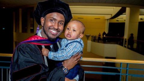 Aj Awer is dressed in cap and gown, posing for a photo with his son