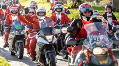 Picture of a previous year's event with several motorcycle riders dressed as Santa driving past the camera
