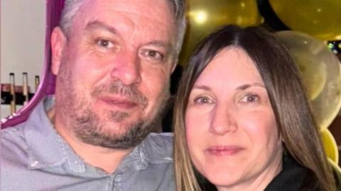 A man with dark hair and a beard in a grey shirt next to a woman with long brown hair and a dark top