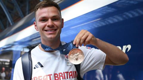 Lewis Richardson holding his Olympic bronze medal after returning home from the Paris Olympics via Eurostar