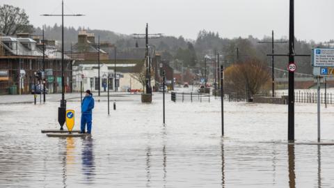 The Whitesands car park and road under flood water with a man wearing blue waterproofs standing on a traffic island
