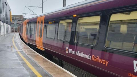 A purple and orange and train in a station. It is branded "West Midlands Railway".