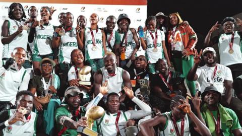 Nigeria's men's and women's victorious flag football teams, with many players wearing medals around their necks or holding them up, pose for a group shot with their trophies at the African Flag Football Championship