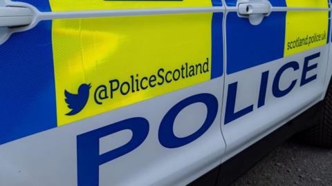 The close up of the side of a Police Scotland car. It has the word "police" and Police Scotland's Twitter/X and website addresses.