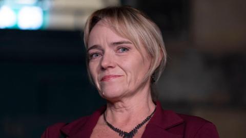 A portrait of a woman, shown from the shoulders up, with a dark background and soft lighting. She has medium-length hair that is neatly styled.