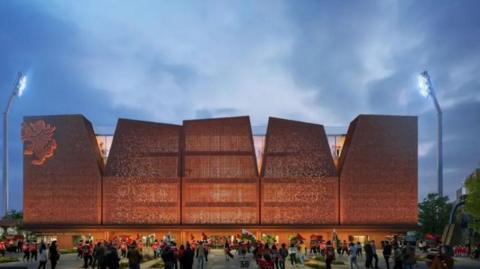 The visual design for the modern-looking Kop stand, its a large building made up of five angular front panels. A red dragon can be seen on the left of the building. Fans holding flags stand infront of the building.