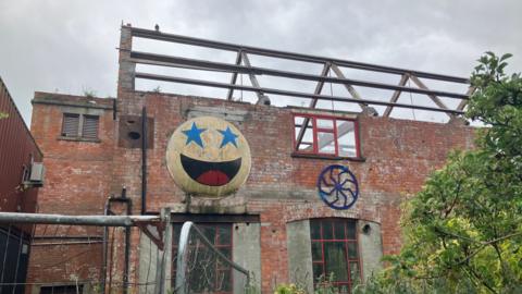 Part of the Life Factory building mid renovation with no roof and a battered smiley face on the side of the building.