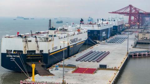 A wide-shot of large ships loading vehicles for export at a port in China