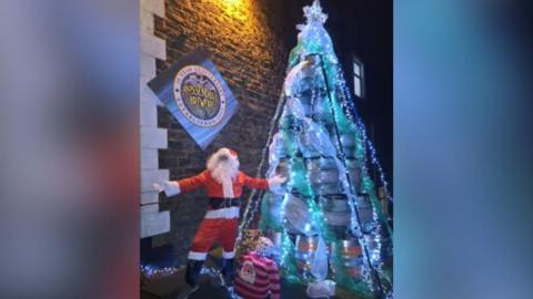Santa stands outside The Griffin Inn with its 4m high illuminated Christmas Tree made out of beer barrels