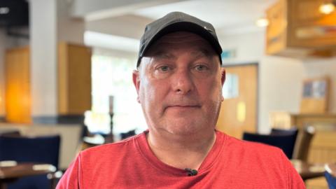 Man wearing a black baseball cap and wearing a red T-shirt looking directly at the camera