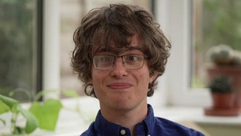 Harry Brown, a teenager with brown wavy hair and glasses, smiles at the camera.