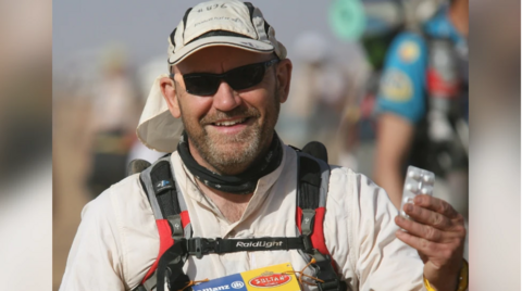 A picture of Dale Thomas wearing sunglasses and a sunhat during a race, carrying what appear to be painkillers in a blister packet.