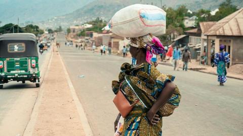 A woman balances a sack of on her head as she crosses a road in Uvira