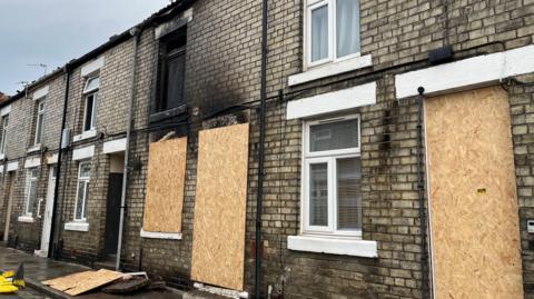 Multiple terraced houses have boarded up ground floor doors and windows after a bad fire. The second floor of one of the homes is blackened.