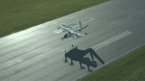 A white electric aircraft with eight propellers takes off on a runway.