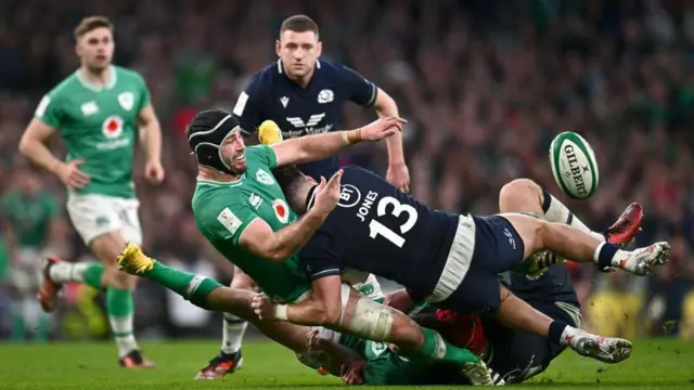 Caelan Doris aig Èirinn a' faighinn caoidhteas a' bhuill fhad 's a tha Huw Jones ga thoirt gu làr le Finn Russell a' coimhead orra.