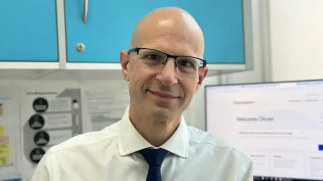A man wearing glasses smiles in a pharmacy office.