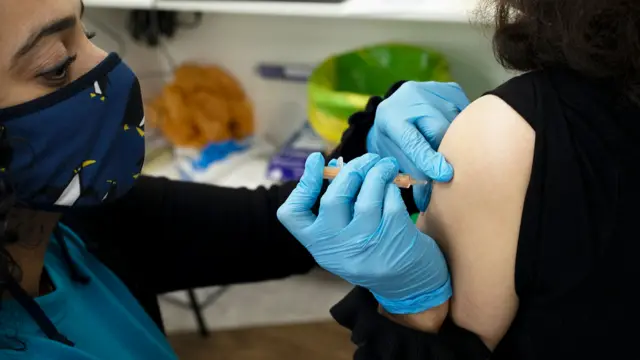 A health professional wearing a blue face mask and blue surgical gloves gives a patient a flu vaccination