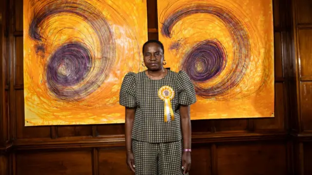 Nnena Kalu stood in front of some yellow and purple paintings
