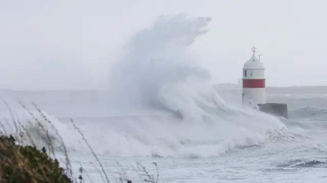A large wave crashes against a lighthouse