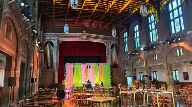 Interior of Bradford Grammar School hall with tables and a stage set up for the ceremony