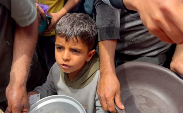 Ismail stands with a pot in a queue for food
