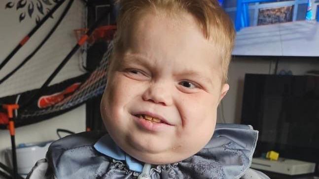 A young boy with fair hair, wearing a grey collared costume.