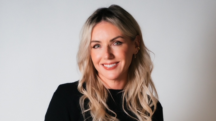 Sali wears a black top and is smiling at the camera. It's a professional headshot. She has long wavy blonde hair.