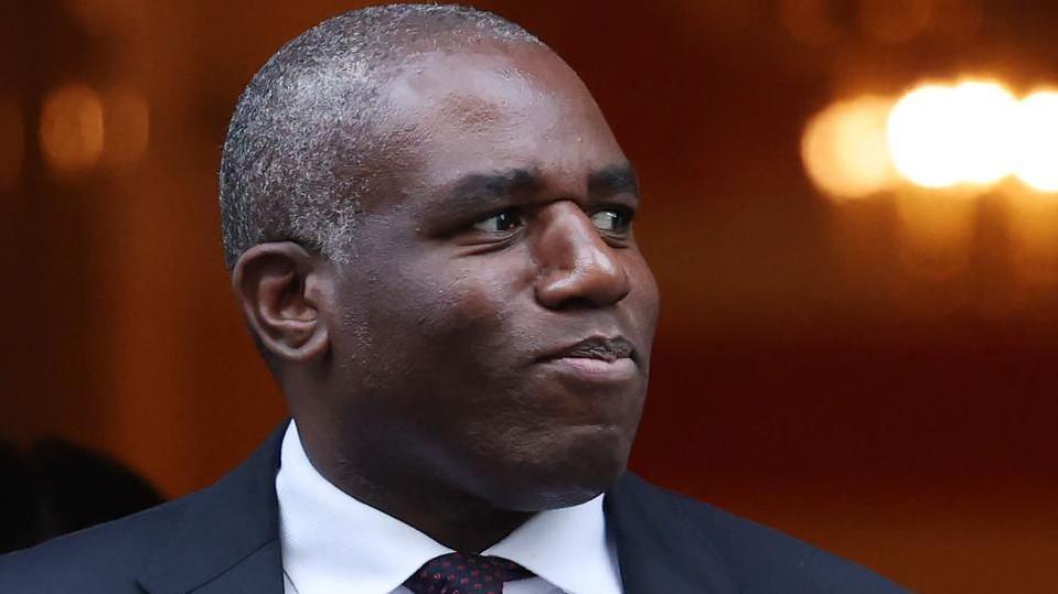 David Lammy, dressed in a suit and tie, looks off to the right.