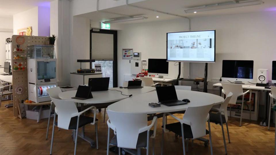 A group of tables with computers laid out at each seat. There is also a projector in the background.