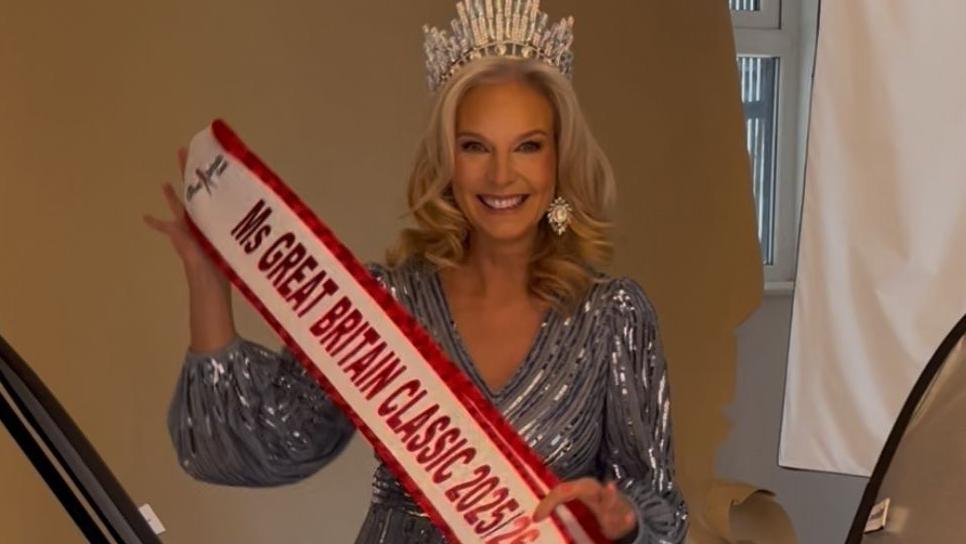 Laura behind the scenes of a photoshoot for Ms Great Britain Classic 2025. She is wearing a blue sparkly dress with a silver tiara and is holding up her sash.