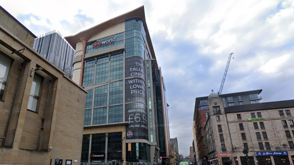 A tall building on the comer of a city street. A large Cineworld sign is prominent at the top of the building.