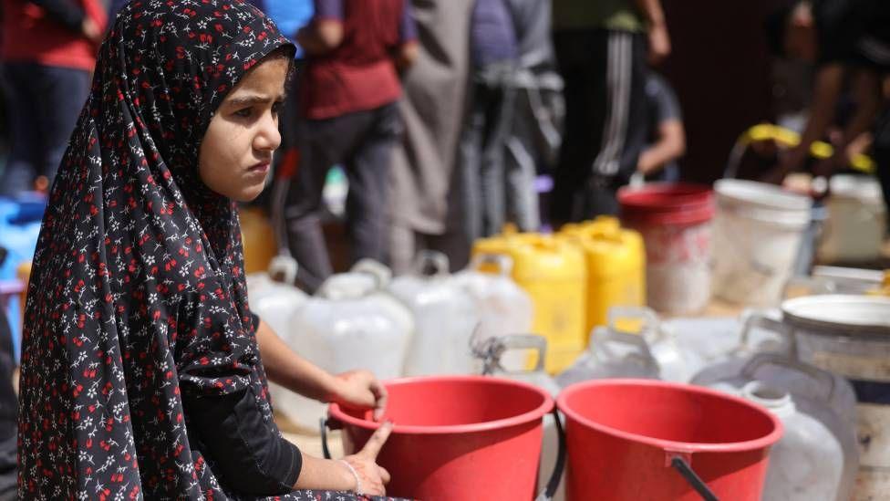 A girl sits next to plastic buckets to collect water in Gaza City