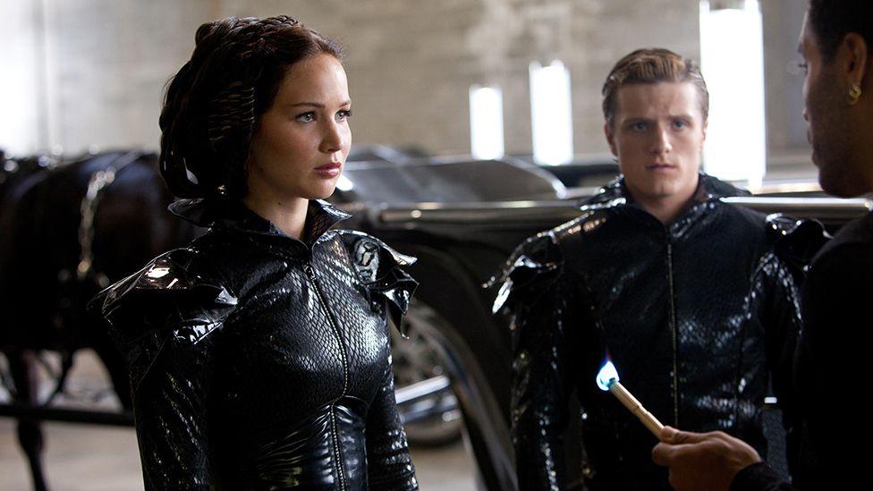 Still from Hunger Games: Mockingjay Part 2 shows Jennifer Lawrence and Josh Hutcherson in costume, being addressed by a third character just off-screen.