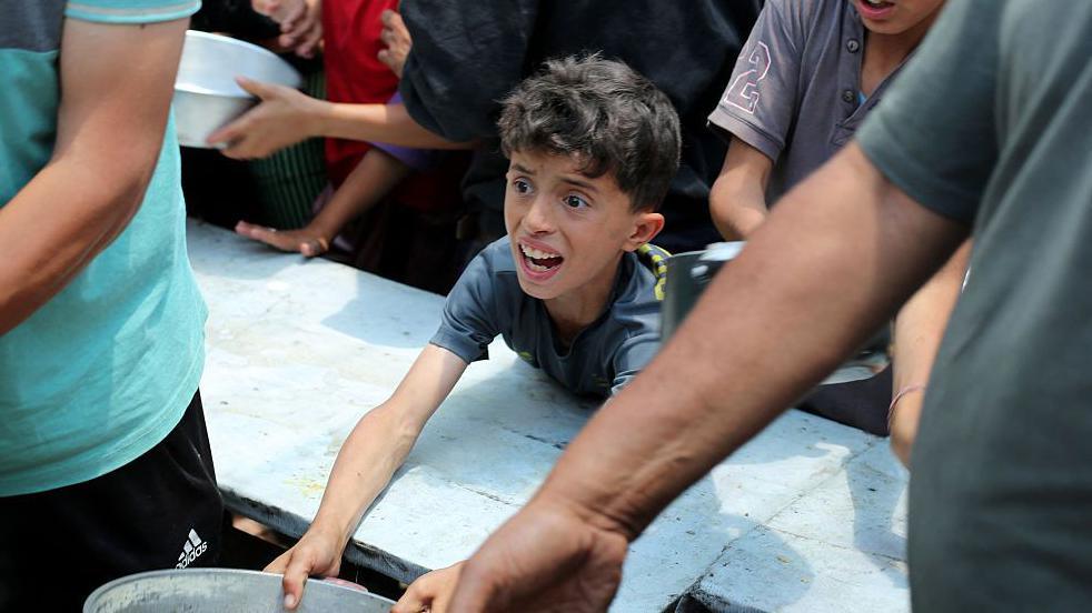 Palestinians gather for a hot meal at a food distribution point in the Nuseirat camp for refugees in the central Gaza Strip on May 21, 2025. Gazans waited desperately for vital supplies on May 21 after Israel said it let in dozens of UN trucks but faced mounting international pressure to increase the aid flow and abandon its intensified military campaign.