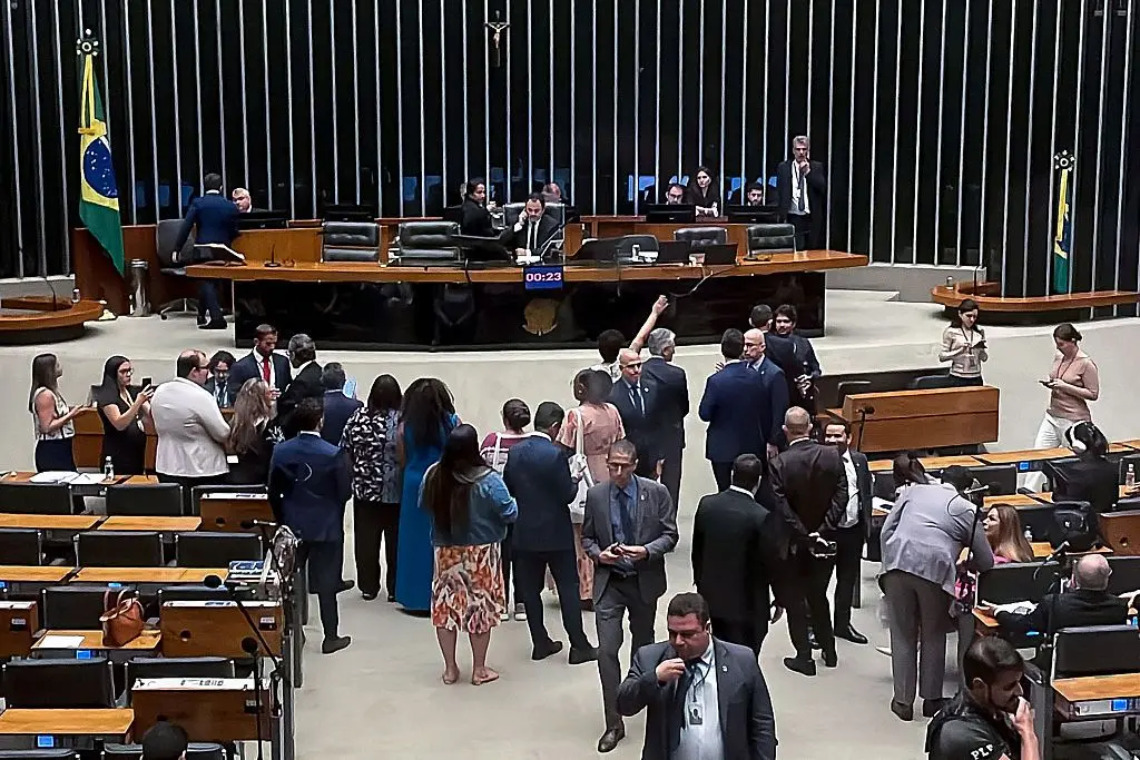 Deputado Glauber Braga sentado na mesa diretora. Parlamentares estão ao redor