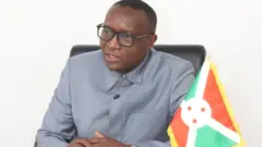 Edouard Bizimana ariko avugana n'abanyamakuru, yambaye amarori, n'ishati ya abacos, imbere y'iwe hari akadarapo k'Uburundi.