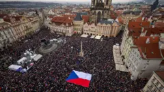 Вид сверху на площадь в Праге, полную людей, с растянутым флагом Чехии.