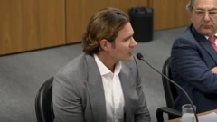 Daniel Vorcaro durante depoimento à Polícia Federal. Ele veste paletó cinza e camisa branca e fala ao microfone