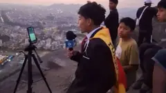 Cliver con un micrófono y el celular en un trípode rodeado de niños en el cerro con vistas al estadio Monumental