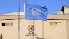 عکسی از پرچم یوناما در کابل، پشت پرچم ساختمان دفتر یوناما دیده میشود.