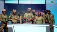 Huit soldats armés en tenue militaire apparaissent derrière le bureau du présentateur du journal télévisé de la chaîne publique béninoise.
