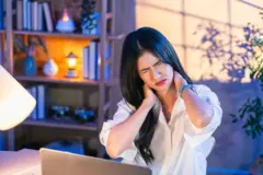 এক নারী চোখ কুচকে দুই হাতে ঘাড় ধরে আছে।