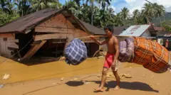 Warga memanggul barang-barang miliknya saat melintas di area banjir bandang dan longsor di Kelurahan Huta Nabolon, Kecamatan Tukka, Kabupaten Tapanuli Tengah, Sumatera Utara, Rabu (3/12/2025).